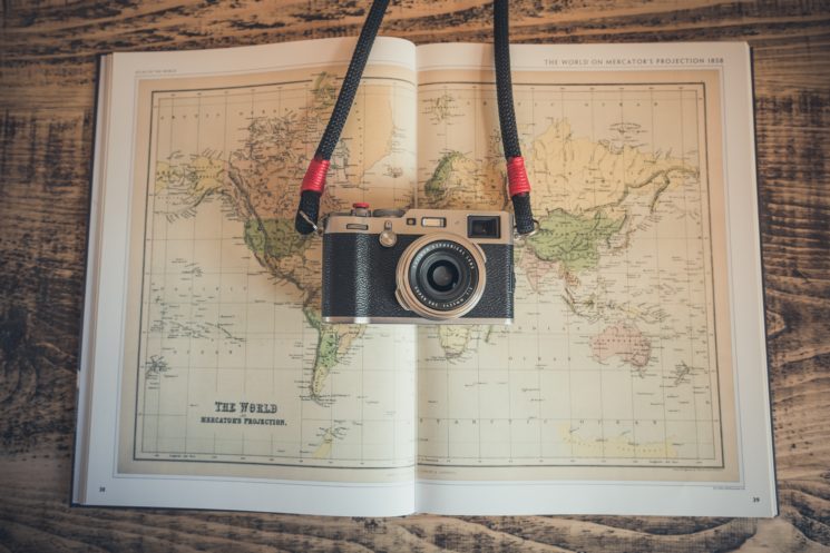A vintage camera resting on an open world atlas on a wooden table, symbolizing travel and exploration