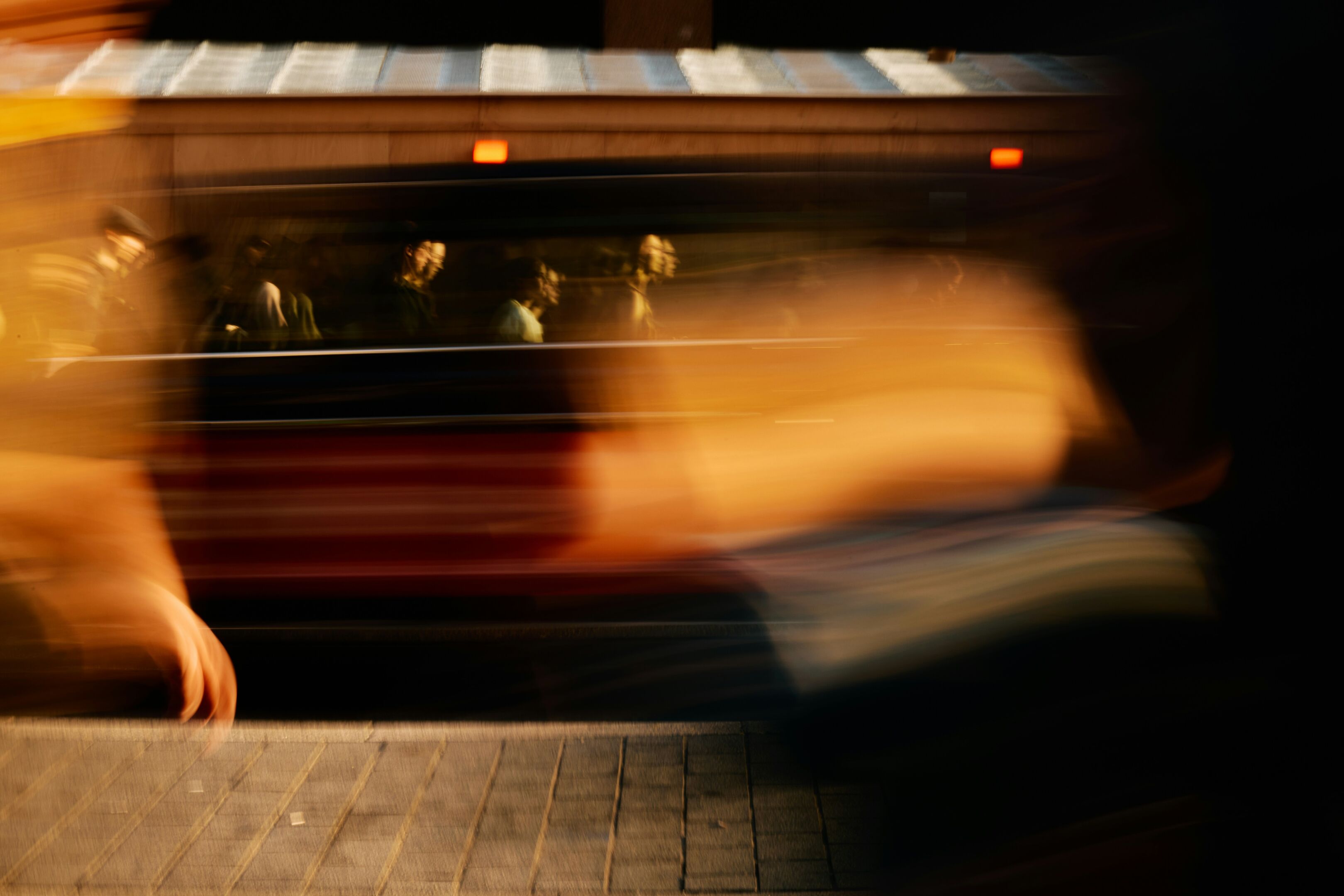 A bus captured in motion blur passing a lit station platform