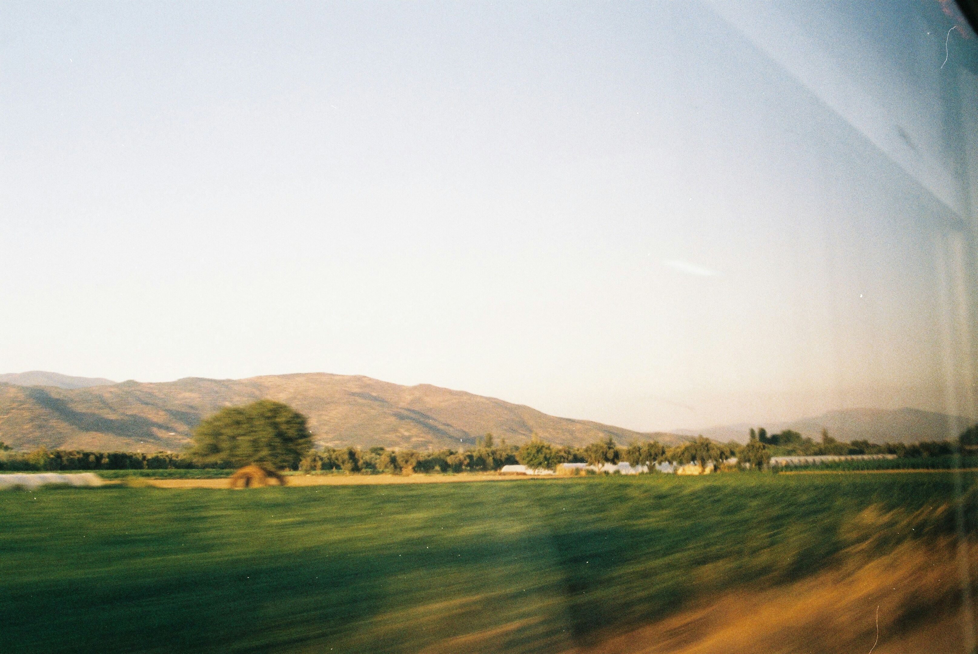 View of fields and distant mountains through a moving train window at golden hour