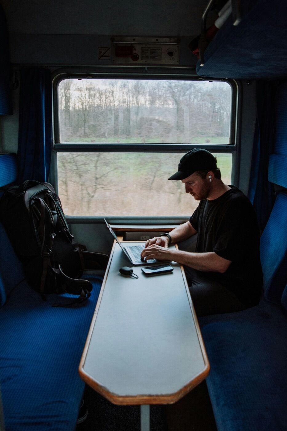 Passenger working on a laptop at a train table with a backpack on the bench across from him