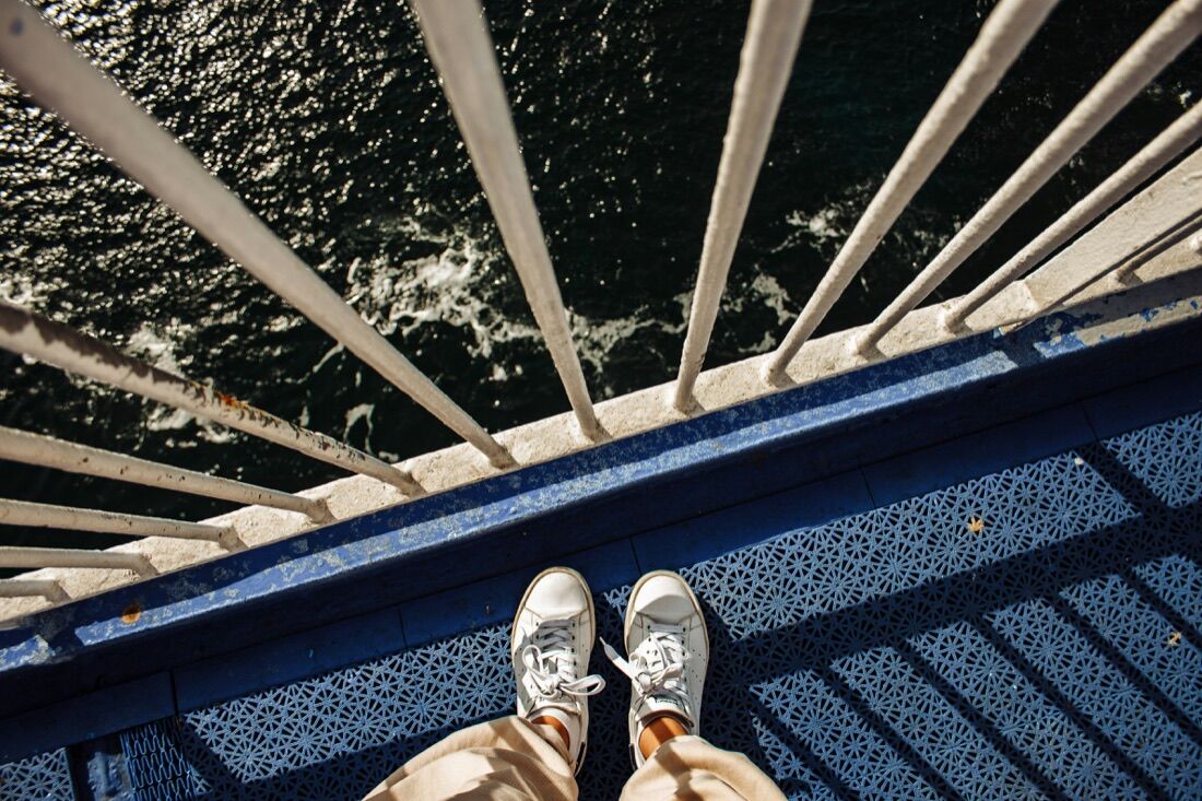 First-person view looking down at sneakers on a ferry deck with the water passing below