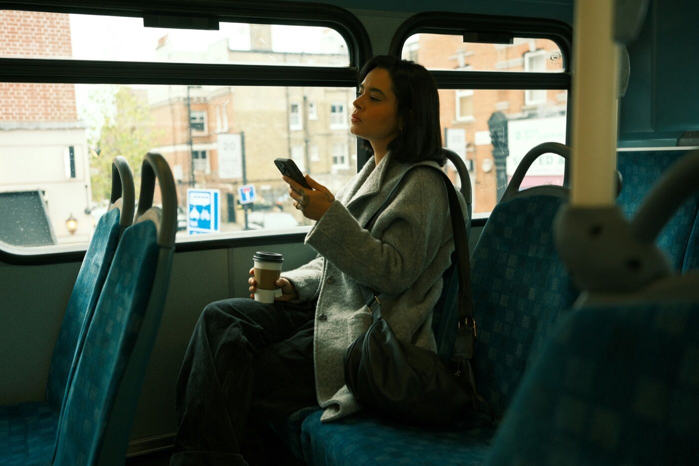 Passenger on a bus holding a coffee and looking at her phone by the window